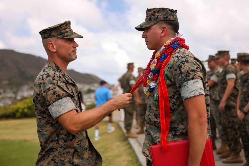 A Marine presents another Marine with an award as other Marines stand behind them.