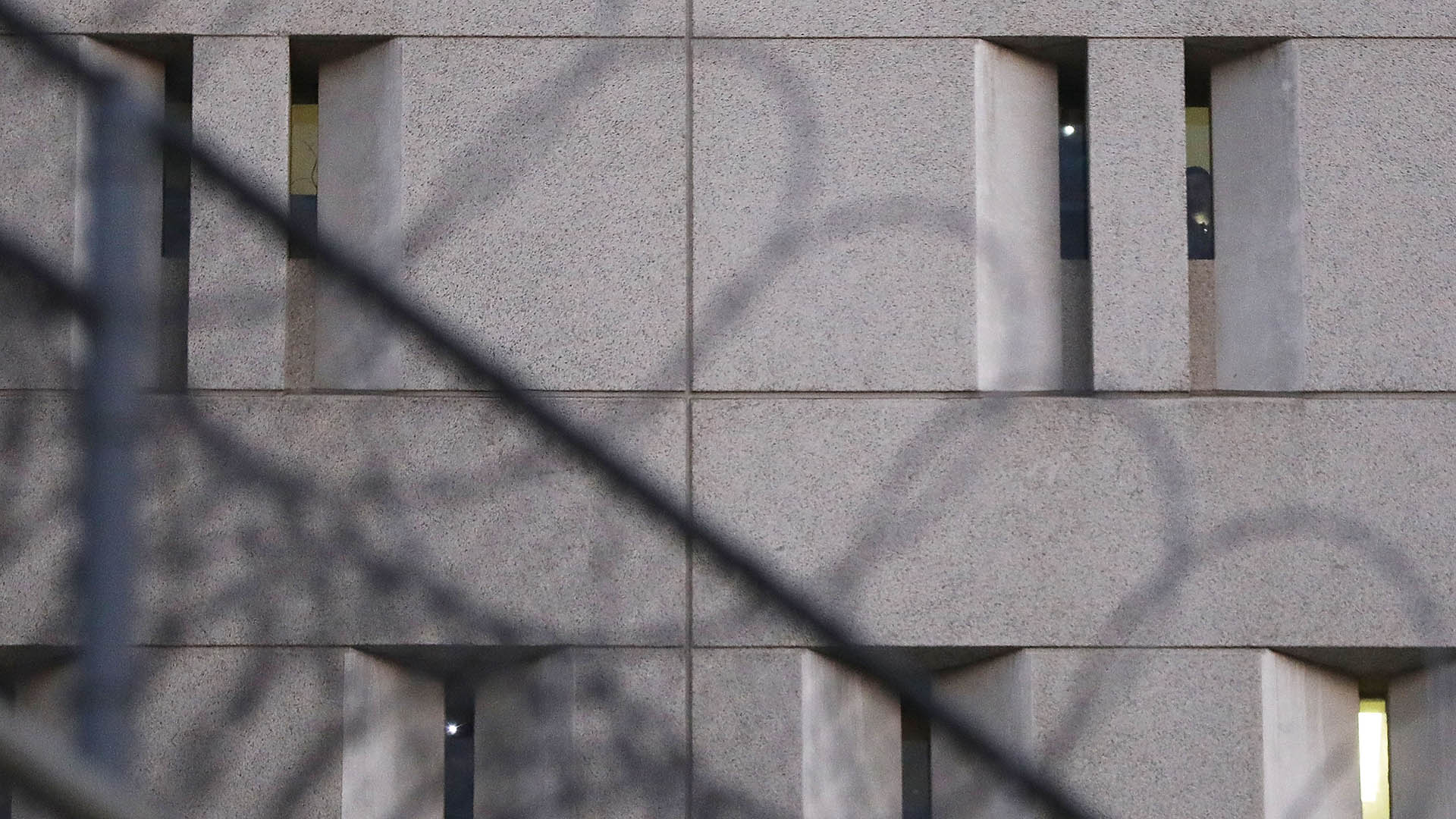 Barbed wire outside a grey immigration detention facility with slit-like windows