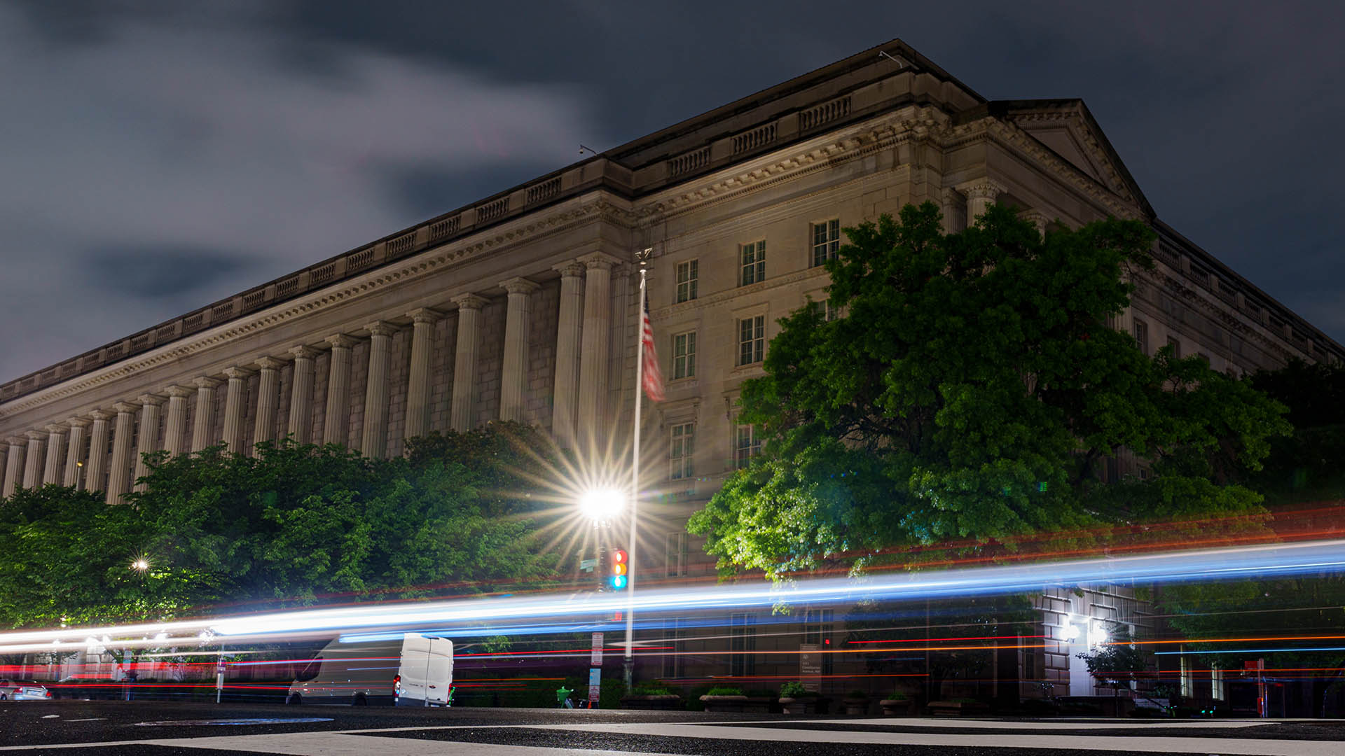 Large office building against a night sky, with streaks of light from the headlights of passing vehicles.