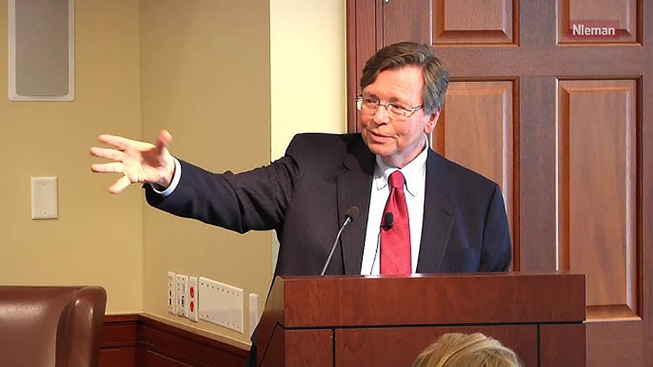 Chuck Lewis gestures with his arm while standing behind a podium