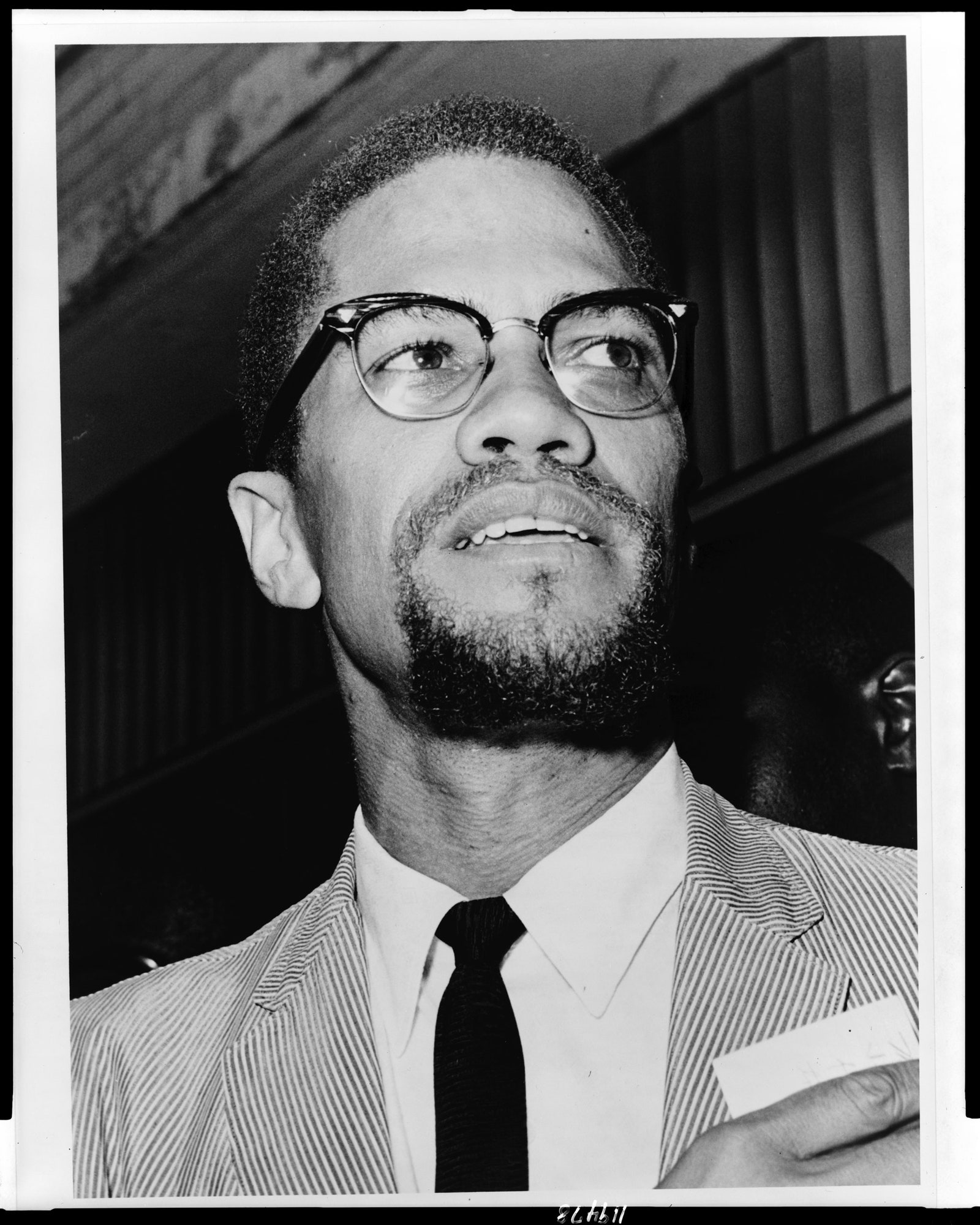 Closeup portrait of Malcolm X from a lower angle as he looks off in to the distance