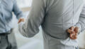 Close up of unrecognizable businessman holding his fingers crossed while shaking hands with his colleague.