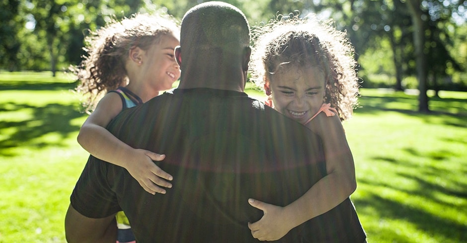 Man laughing with two daughters in a park