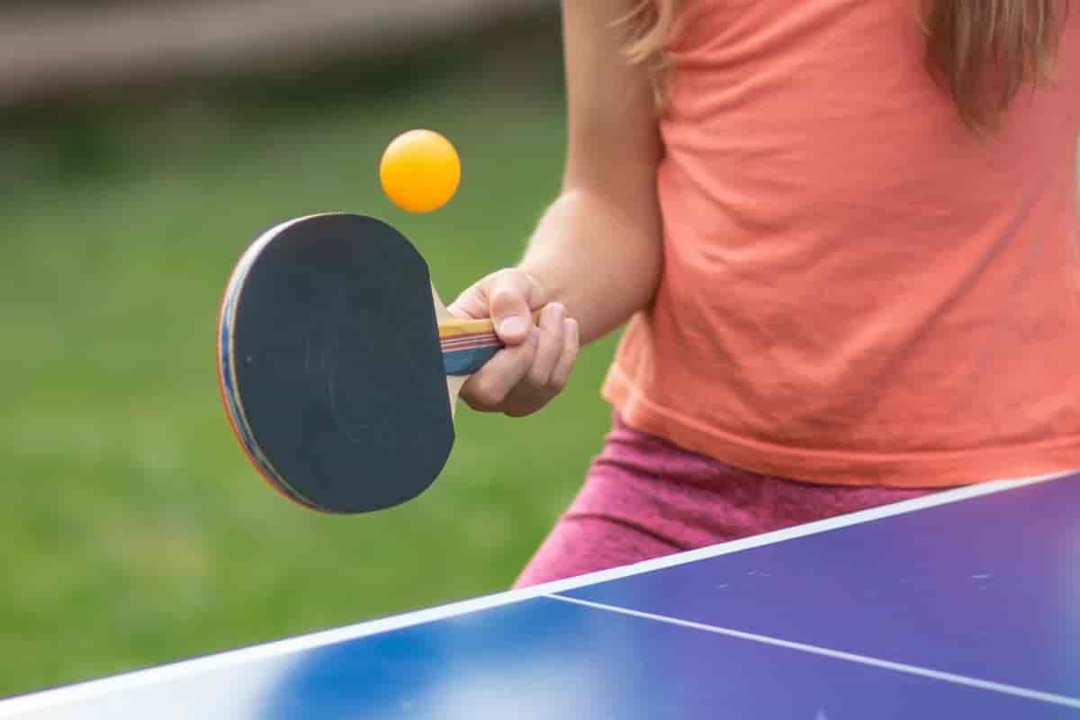 Foto av en hånd som holder en bordtennisracket ved kanten av et bordtennisbord. En ball er i lufta rett ved racketen. 