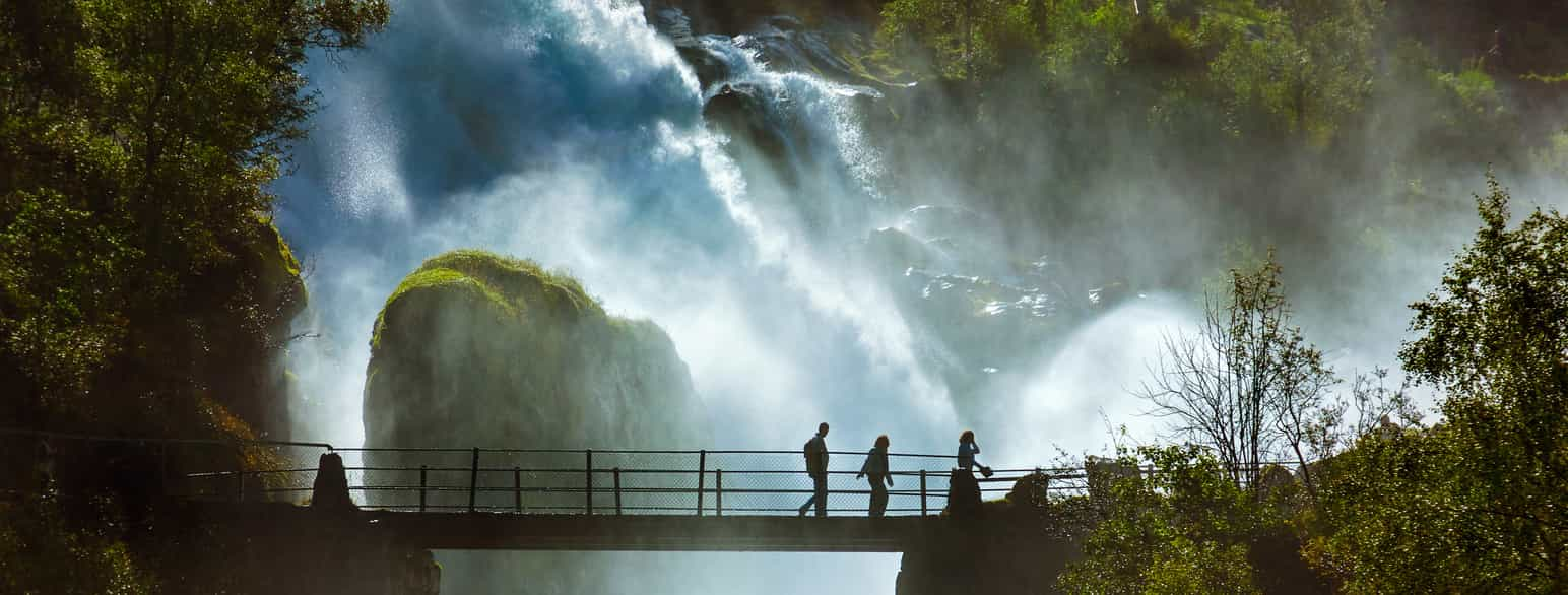 Foto av folk som går over en bro ved en bratt foss