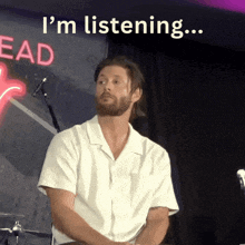 a man in a white shirt is sitting in front of a sign that says ' i 'm listening '