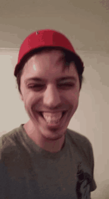 a man wearing a red hat and a grey shirt is smiling and sticking his tongue out