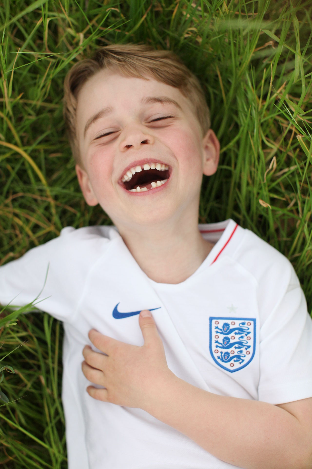 Image may contain Human Person Face Smile Grass Plant Clothing Apparel Prince George of Cambridge and Laughing