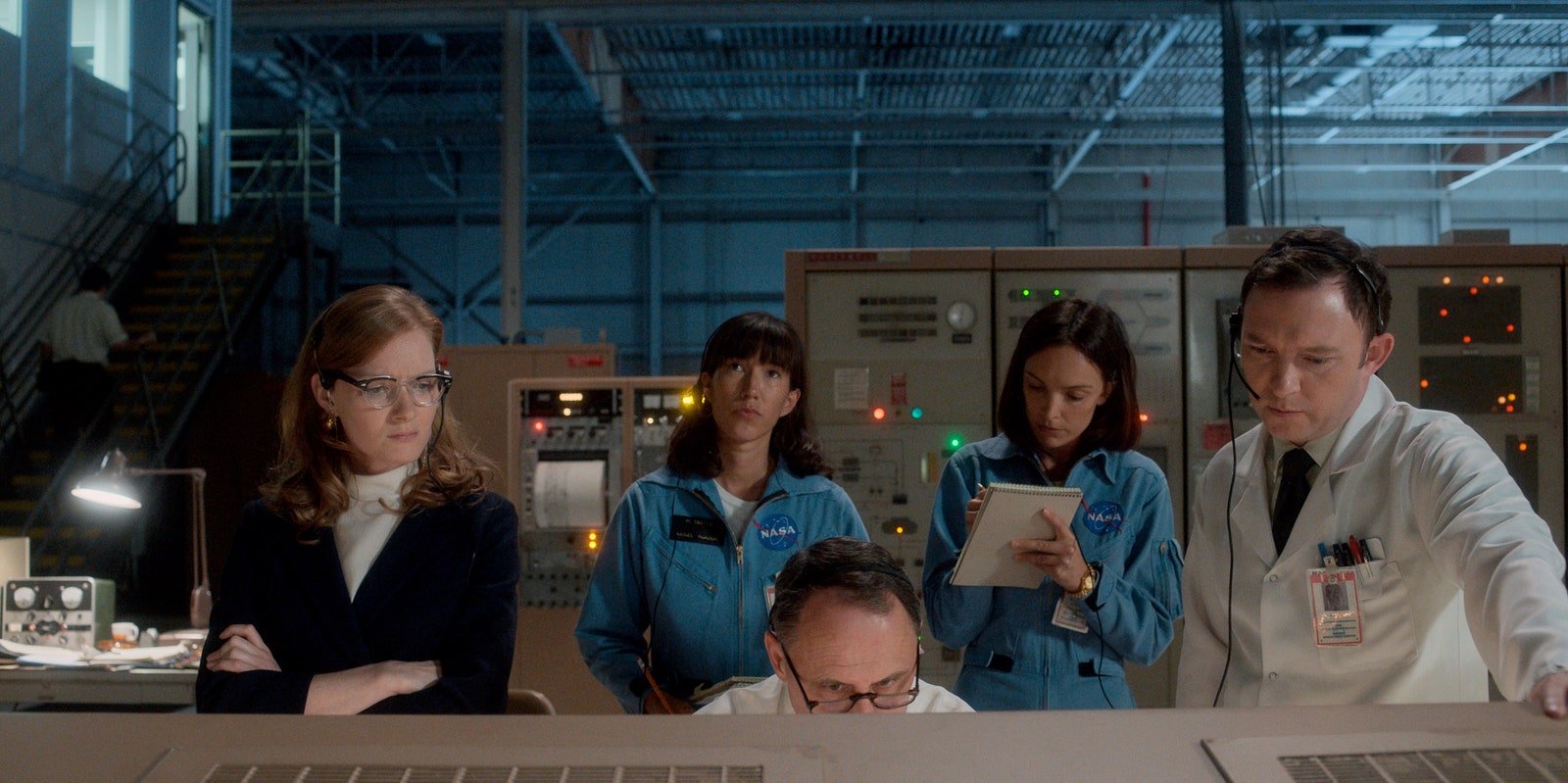 People stand around a man looking at a screen in a scene from For All Mankind