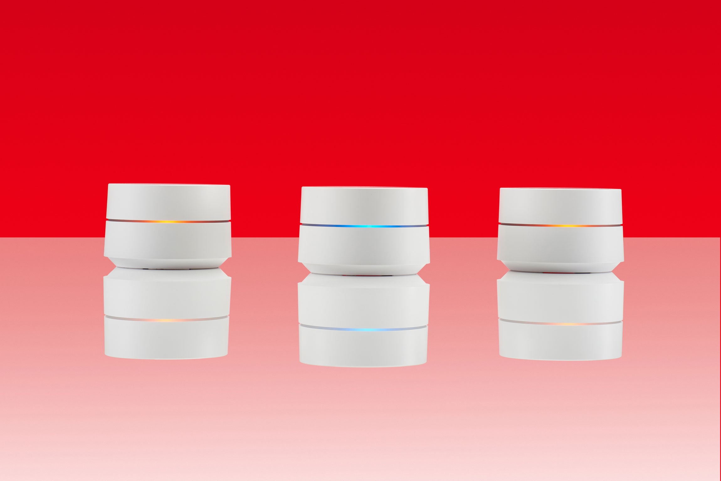 three google home routers against red backdrop and reflected on table