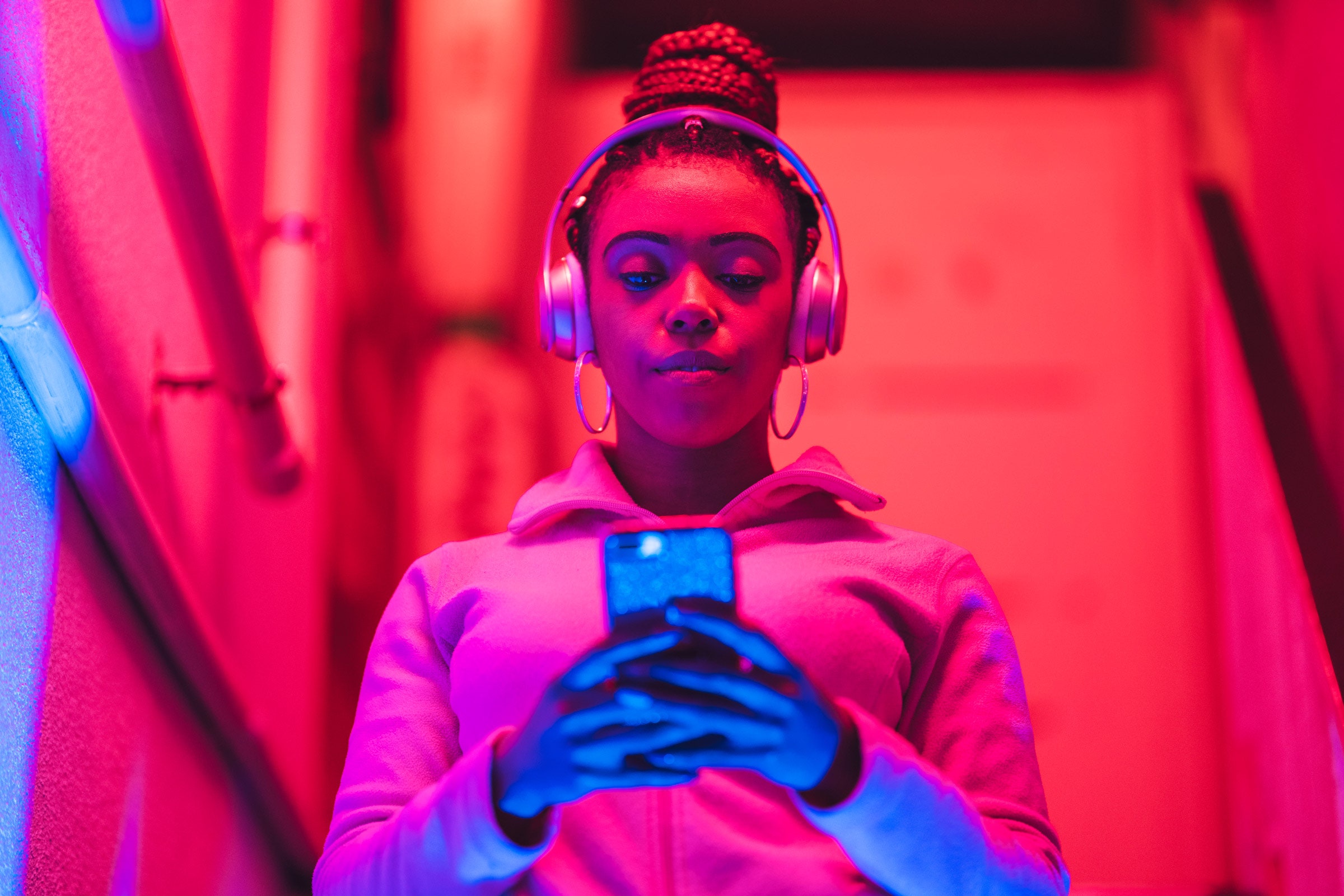 a Black woman looking at her phone and listening to music through headphones