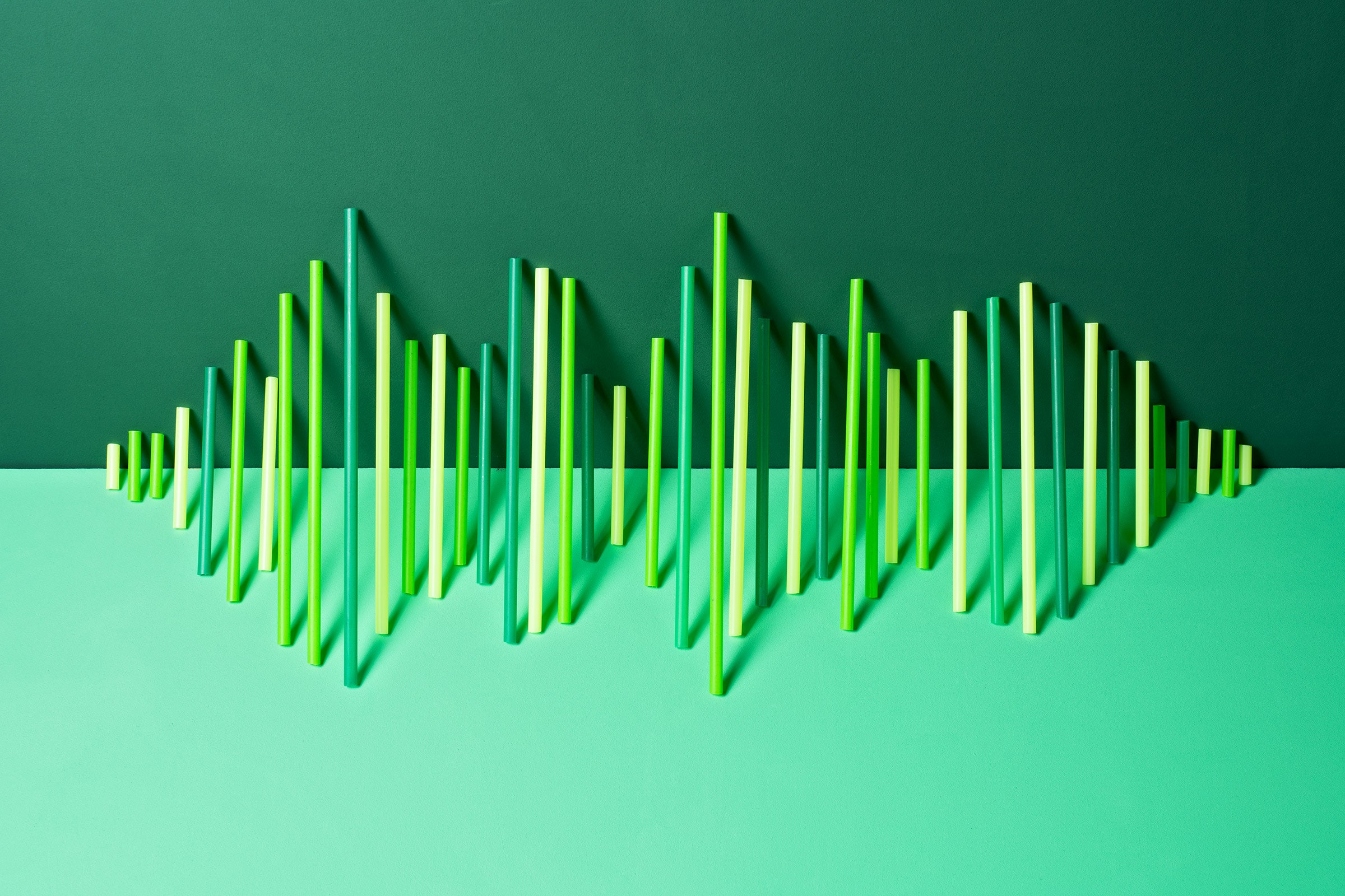 Uneven green plastic straws lined up on green backdrop to look like undulating sound waves