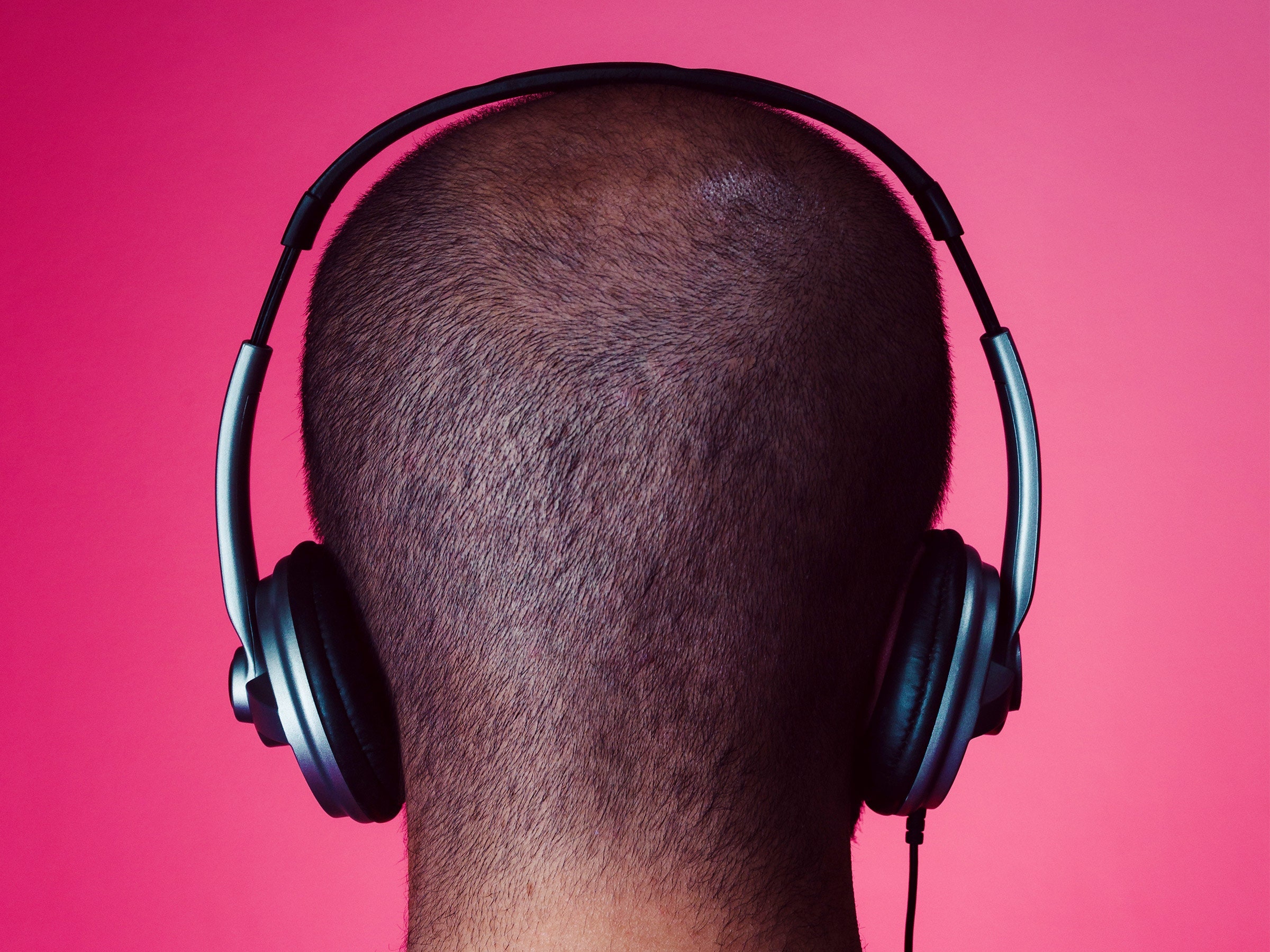 Back of person's head who is wearing overear headphones against pink background