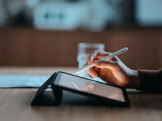 Side view of a hand using a digital tablet on top of a table while holding a stylus