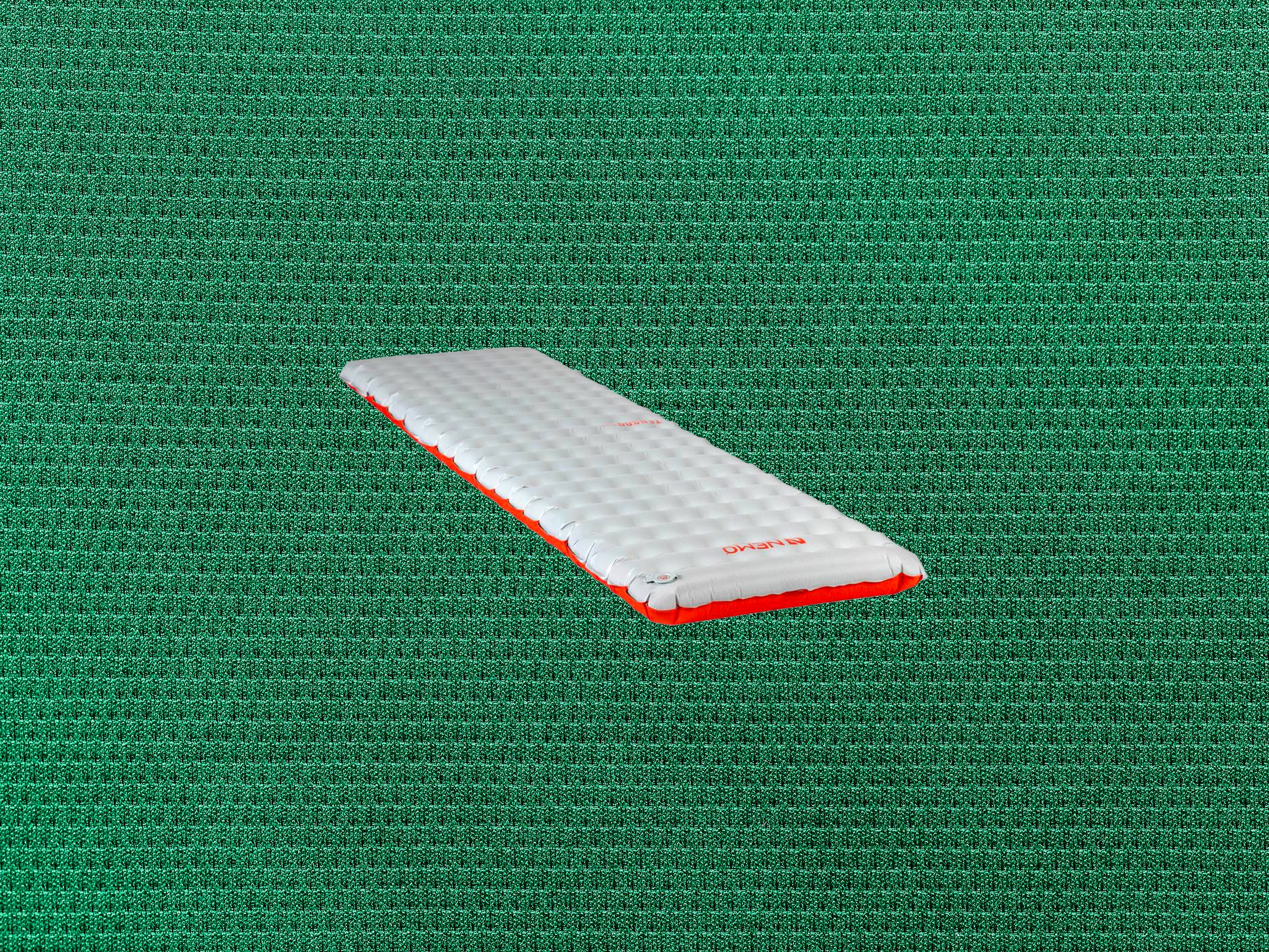 Inflatable sleeping pad with white top and red bottom on a green textured background