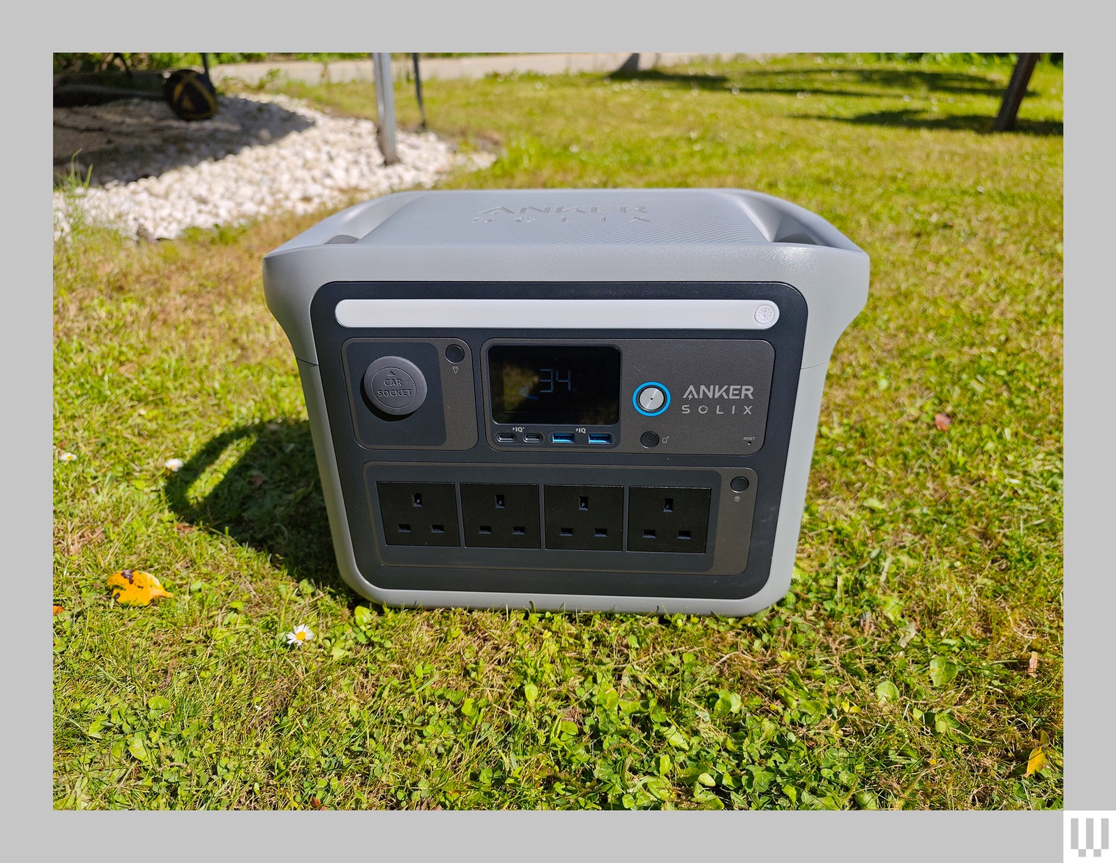 Grey square device sitting in the grass with large handles on each side and outlets screens and button the front