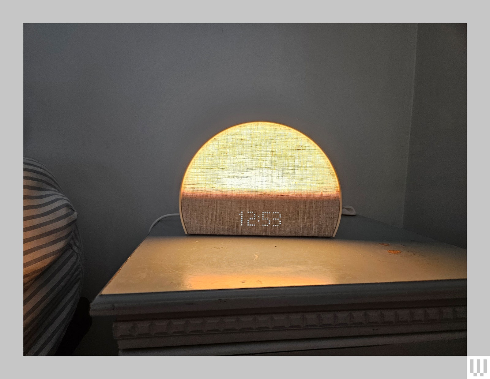 Semicircular shaped clock on nightstand partially illuminated like a rising sun on the horizon