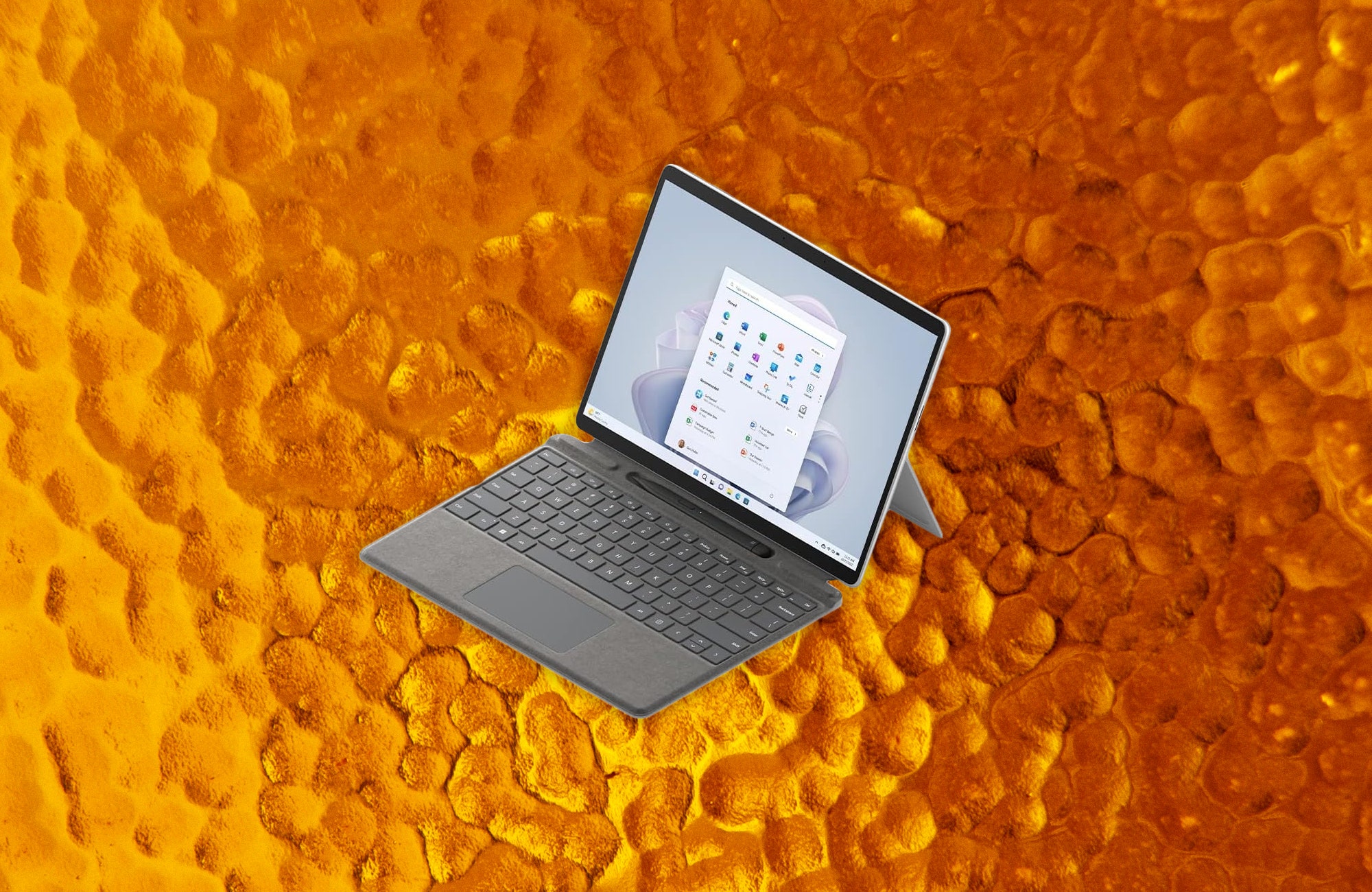 Tablet propped up by a stand connected to a detachable keyboard. Background yellow and orange dented glass.