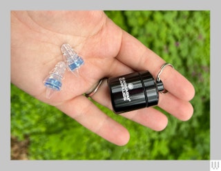 Hand holding small black canister on a keyring and 2 clear ear cushions