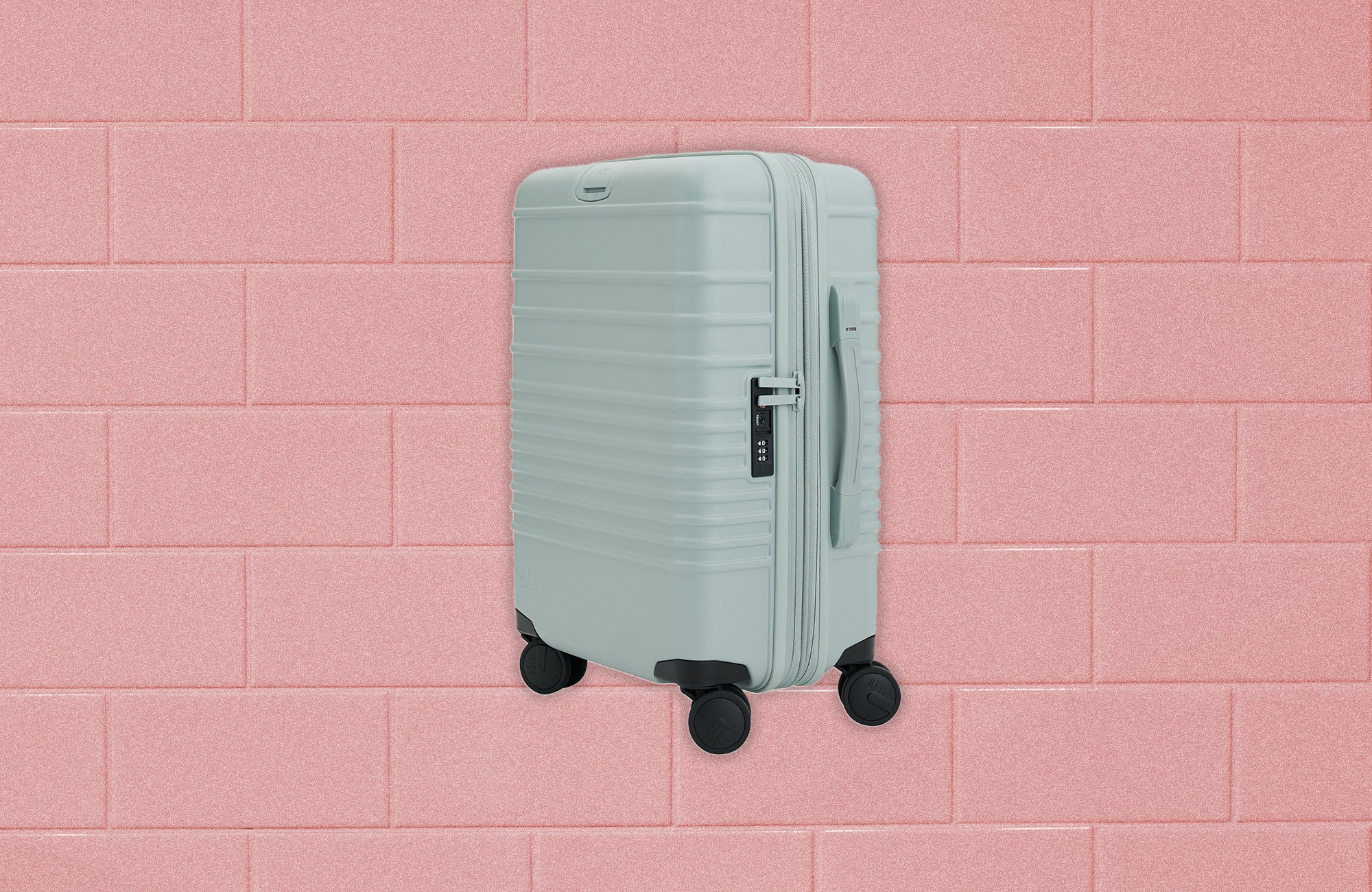 Small rectangular rolling luggage case with rounded corners and a long metal handle extended upward. Background Pink...