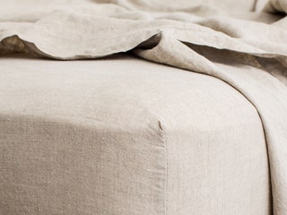 Closeup of the corner of a mattress with beige linen sheets