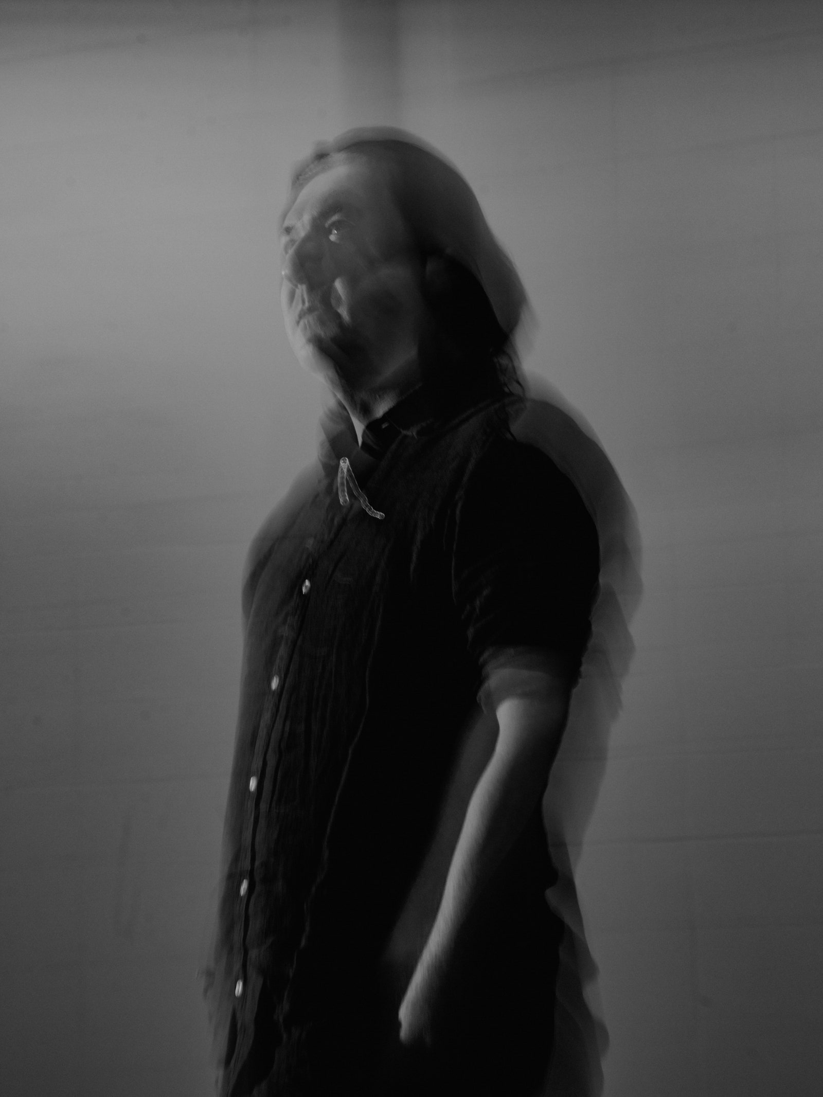A black and white motion blur portrait of a person with long dark hair who is wearing a dark button up shirt