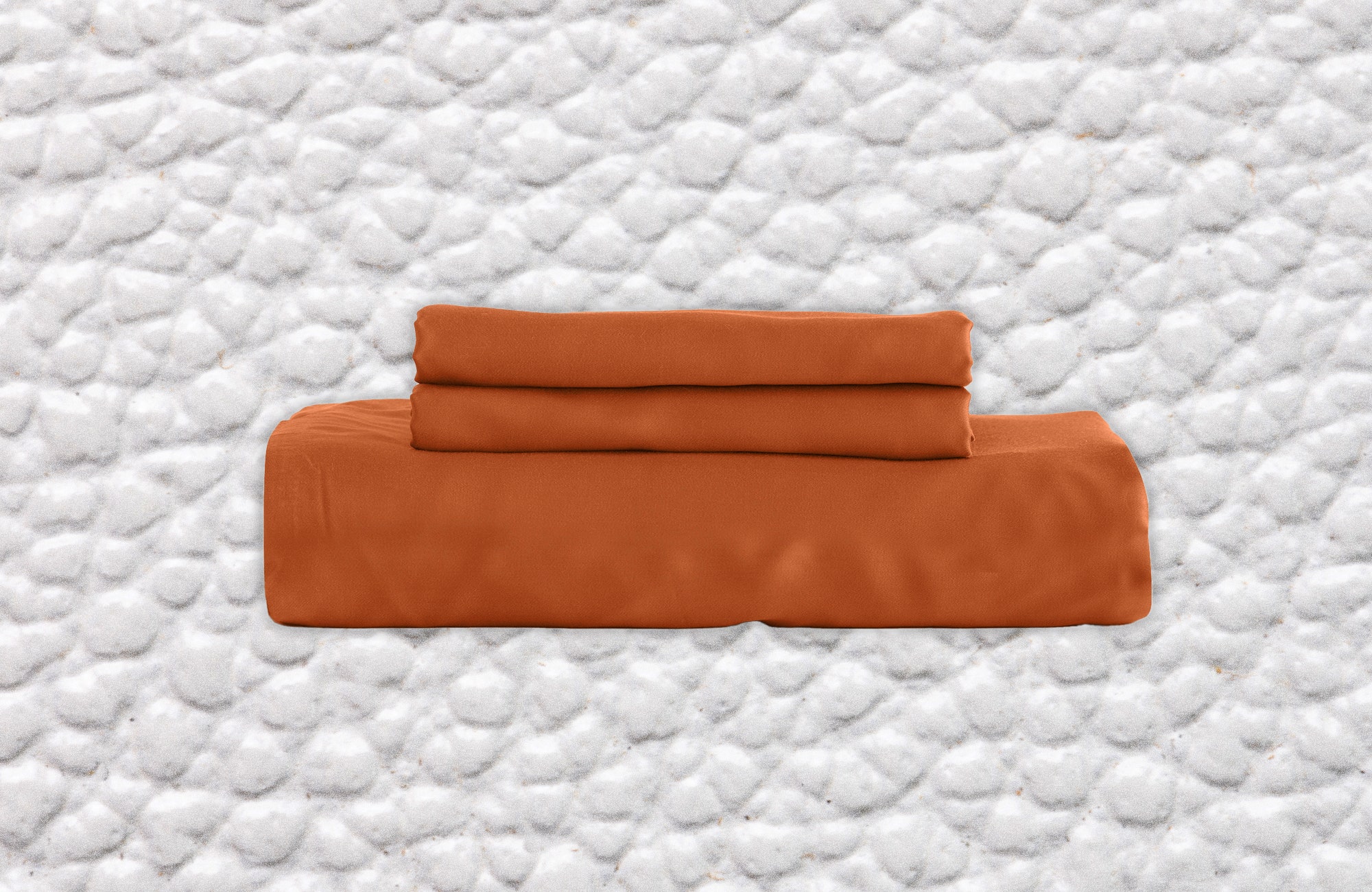 Stack of terracotta colored bed sheet and pillowcases. Background white leather texture.
