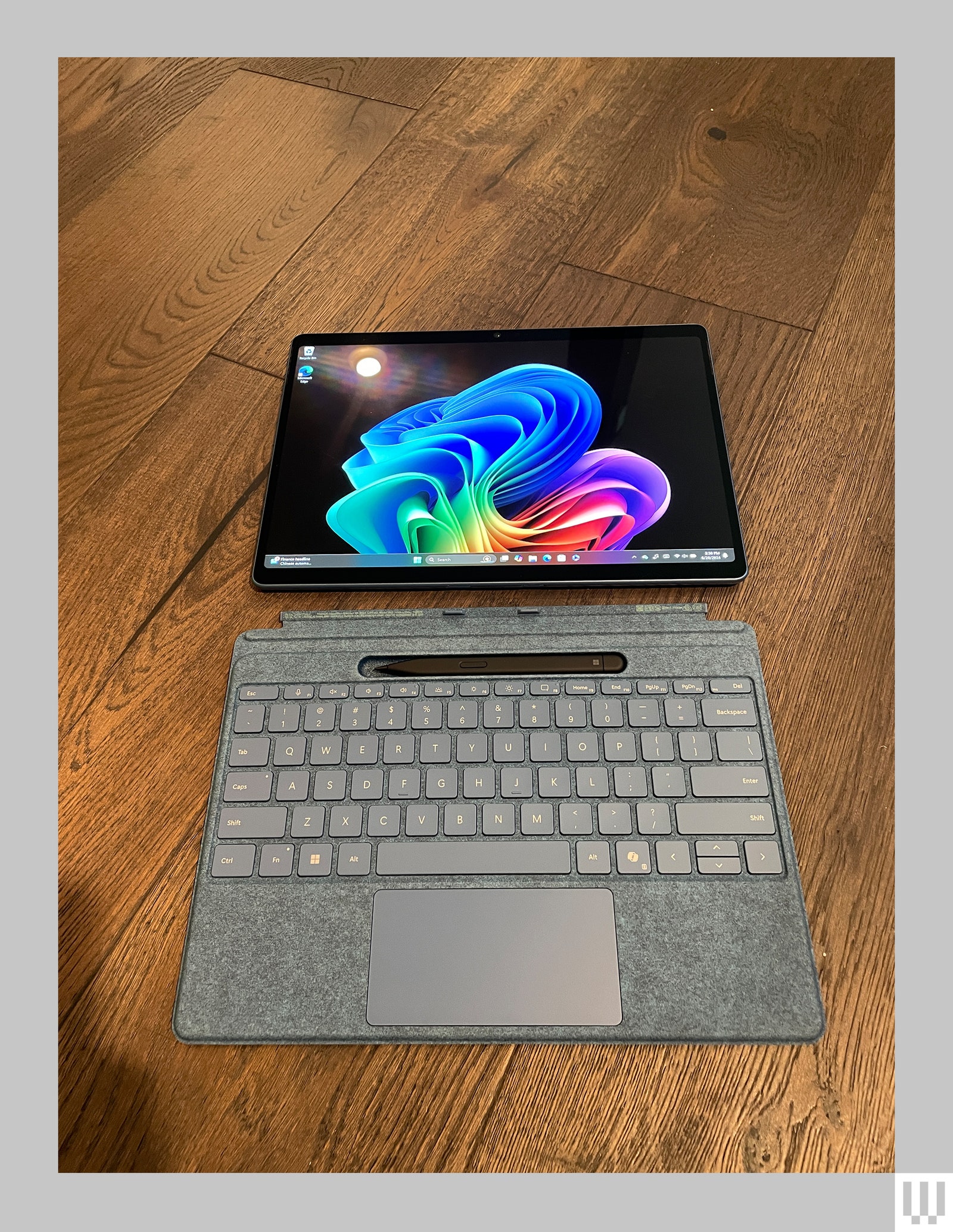Tablet laying flat on a wooden floor separate from a detachable keyboard and stylus
