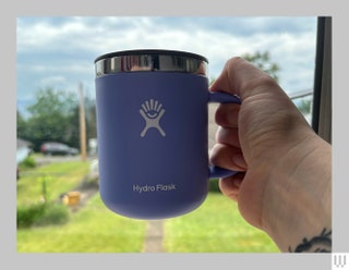 Hand holding up a blue mug with silver rim in front of an open door with a lawn in the distance