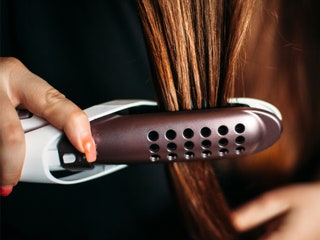 Closeup of someone using a white and burgundy hair straightener on reddish brown hair