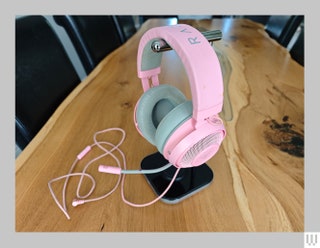 Pink headphones with a mic protruding on a silver stand sitting on a wooden table