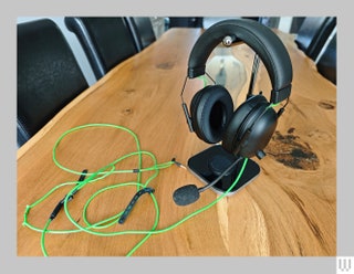 Black padded headphones with a green cord and protruding mic hanging from a silver stand