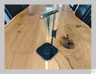 Silver stand with black base for charging headphones sitting on wooden table