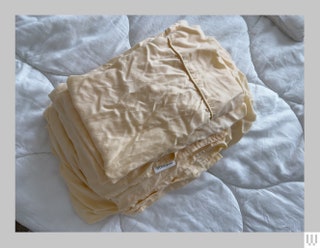 Stack of wrinkled peach colored sheets on a white comforter