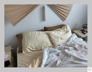 Overhead view of a bed partially made with two fluffy pillows and wrinkled sheets and blanket