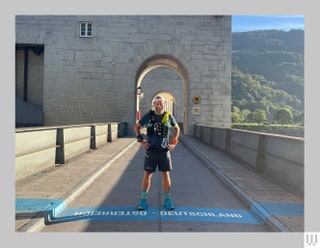 Person in tshirt shorts running shoes and backpack standing on a stone bridge at the border between Austria and Germany