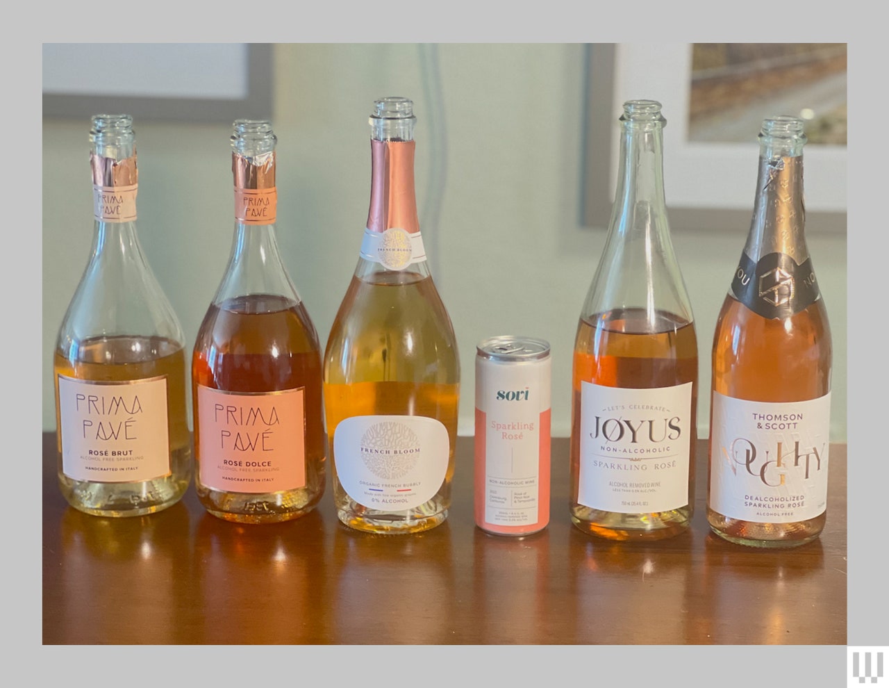 5 bottles of nonalcoholic beverages with light colored liquid inside and a white can, sitting on a wooden table 