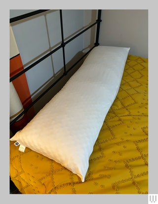 Long white pillow laying across the top of a bed with a yellow blanket underneath