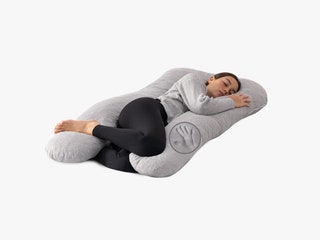 Person curled up with a ushaped grey pillow wrapping around their body from back to front and head to toes