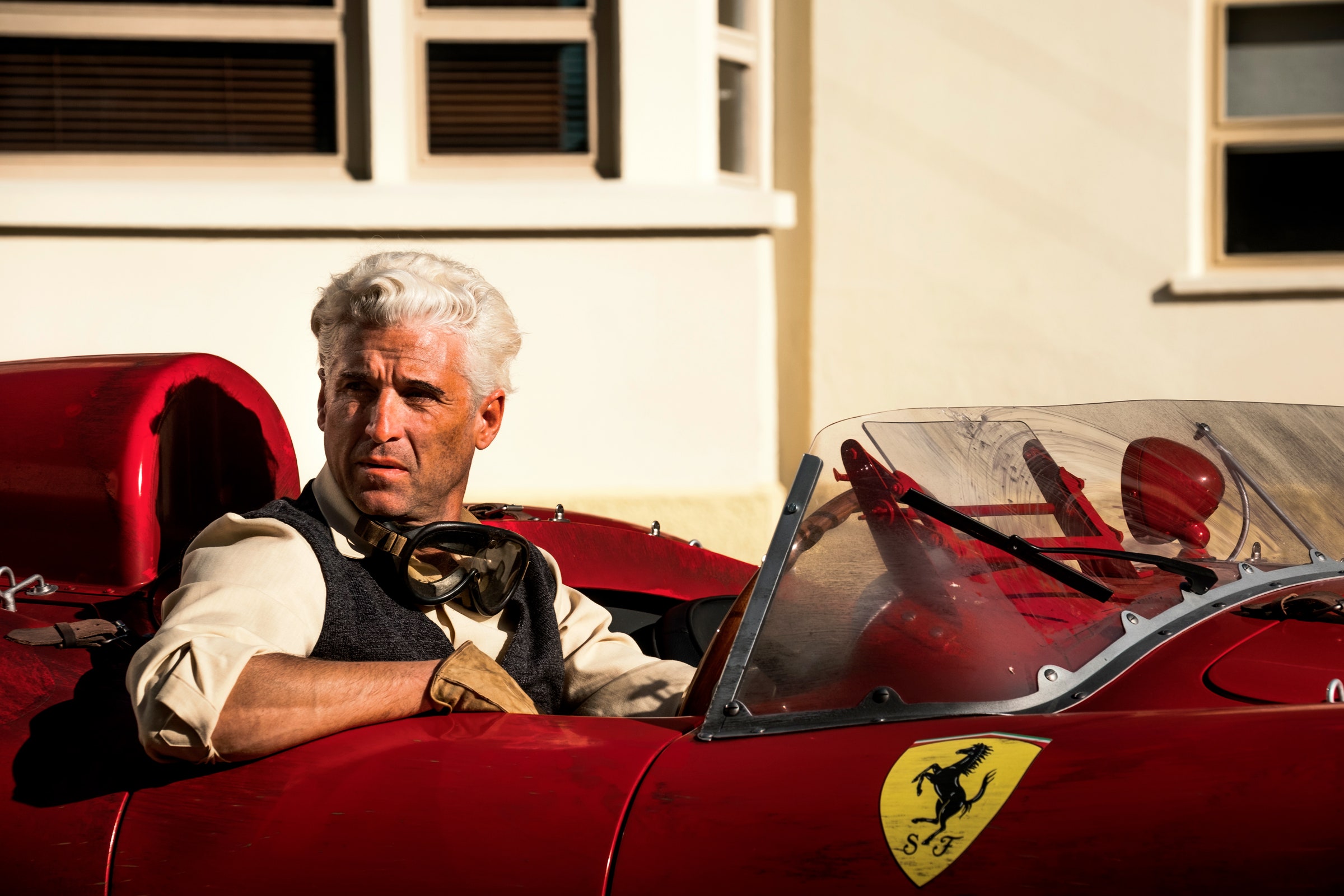 An image of Patrick Dempsey as Piero Taruff sitting in a red Ferrari in the film 'Ferrari.'