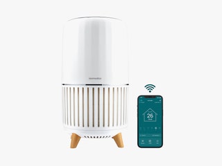 White cylindrical air purifier beside a mobile phone with the screen showing an app for air quality