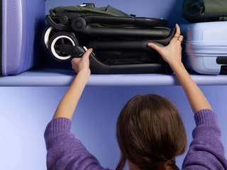 Person in purple sweater putting a folding strollerpram in the aircraft overhead cabin beside other luggage