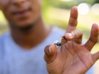 Person outdoors with their hand pinching a small hearing aid in the foreground