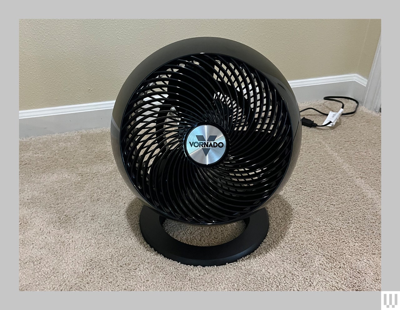 Small black circular fan sitting on a carpeted floor of a room