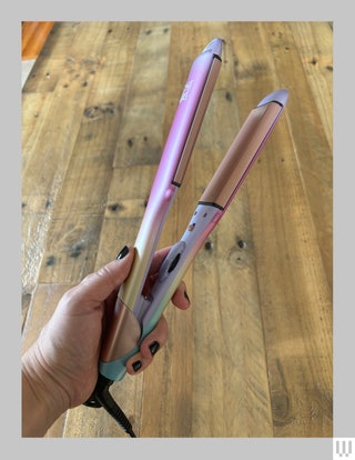 Hand holding a thin purple and iridescent hair straightener showing a pink colored panel on the inside of one of the clamps