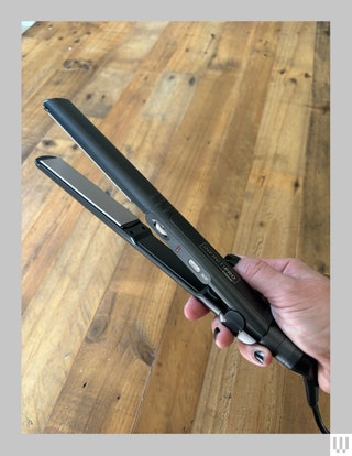 Hand holding a thin black hair straightener showing a silver colored panel on the inside of one of the clamps