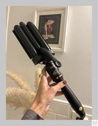 Hand holding the Amika High Tide Deep Waver a curling iron with three barrels bulbous center with digital screen and...