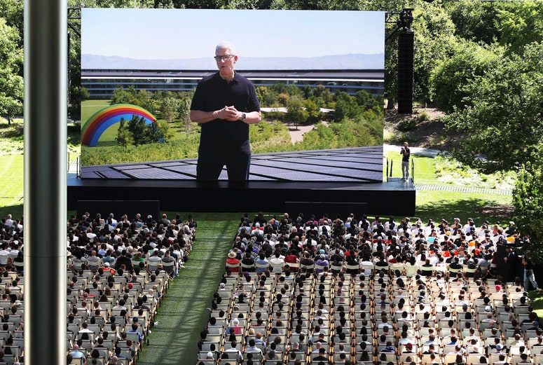 A crowd of WWDC attendees watching Tim Cook speak on a large screen 