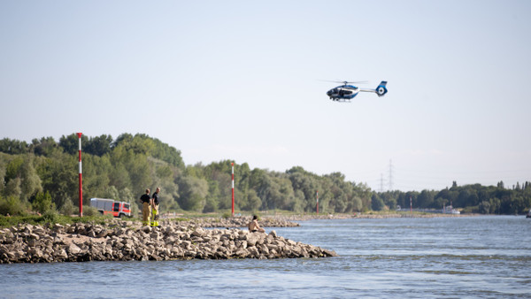 Aus einem Hubschrauber und vom Ufer aus suchen Einsatzkräfte nach einem Schwimmer, der im Rhein von einem Sog erfasst und mitgerissen wurde.