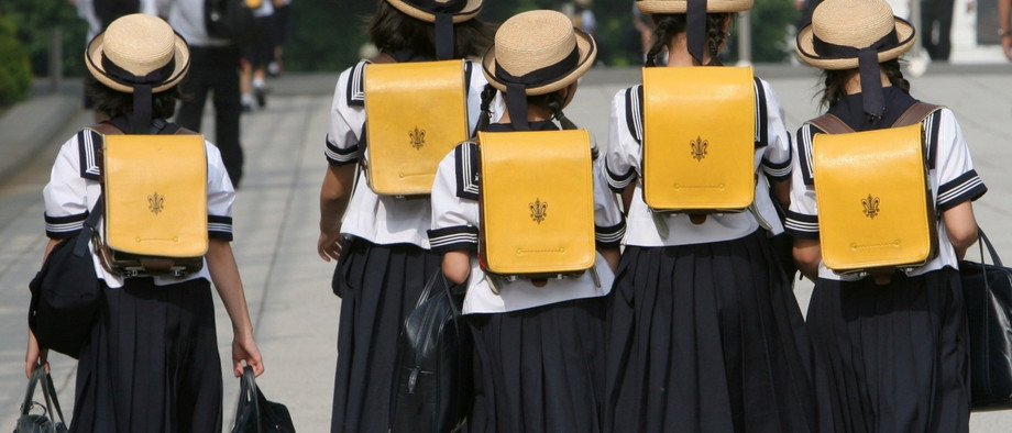 Japanische Mädchen laufen in Tokio in Schuluniforn auf einer Straße.